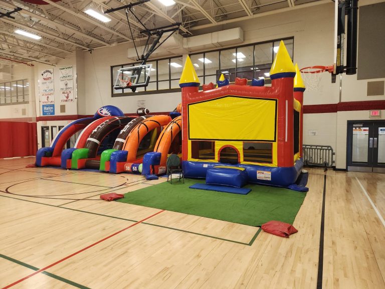 Birthday party setup in YMCA gymnasium featuring MaxAiir inflatable slide, bounce house, tables, and chairs with kids playing and celebrating
