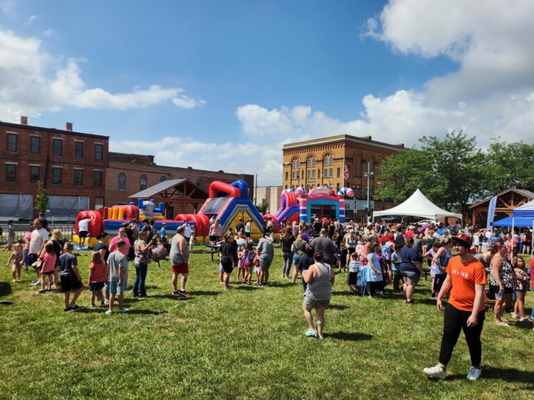 Large crowd enjoying MaxAiir inflatables and bounce houses at Buzzes & Backpacks 2024 in downtown Marion, Ohio under sunny skies