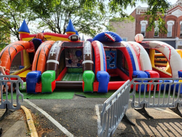 Multi-sport inflatable games including basketball, football, baseball, and soccer set up outdoors by MaxAiir Party Rentals with safety barricades in front