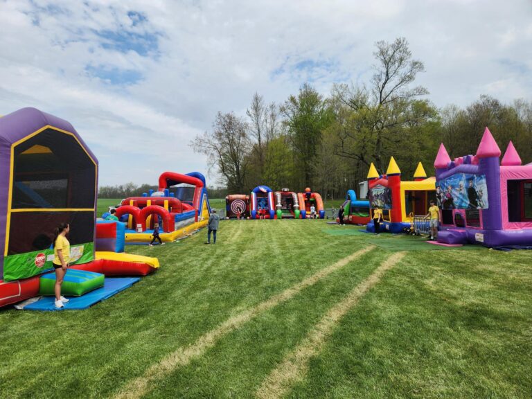 Wide view of MaxAiir’s outdoor inflatable rentals setup at Earth Day Eco Center 2024, with obstacle courses and character bounce houses on grass field