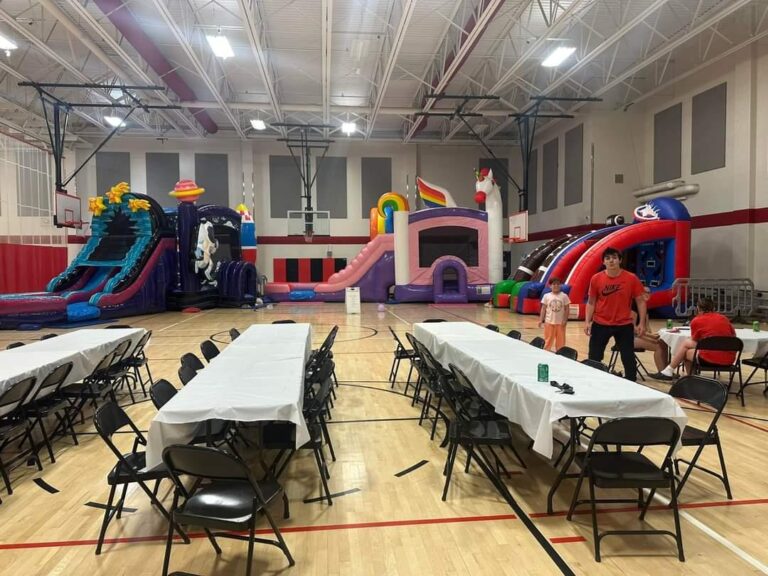 YMCA gymnasium party setup with MaxAiir inflatable slides, bounce houses, tables, and chairs for kids and families